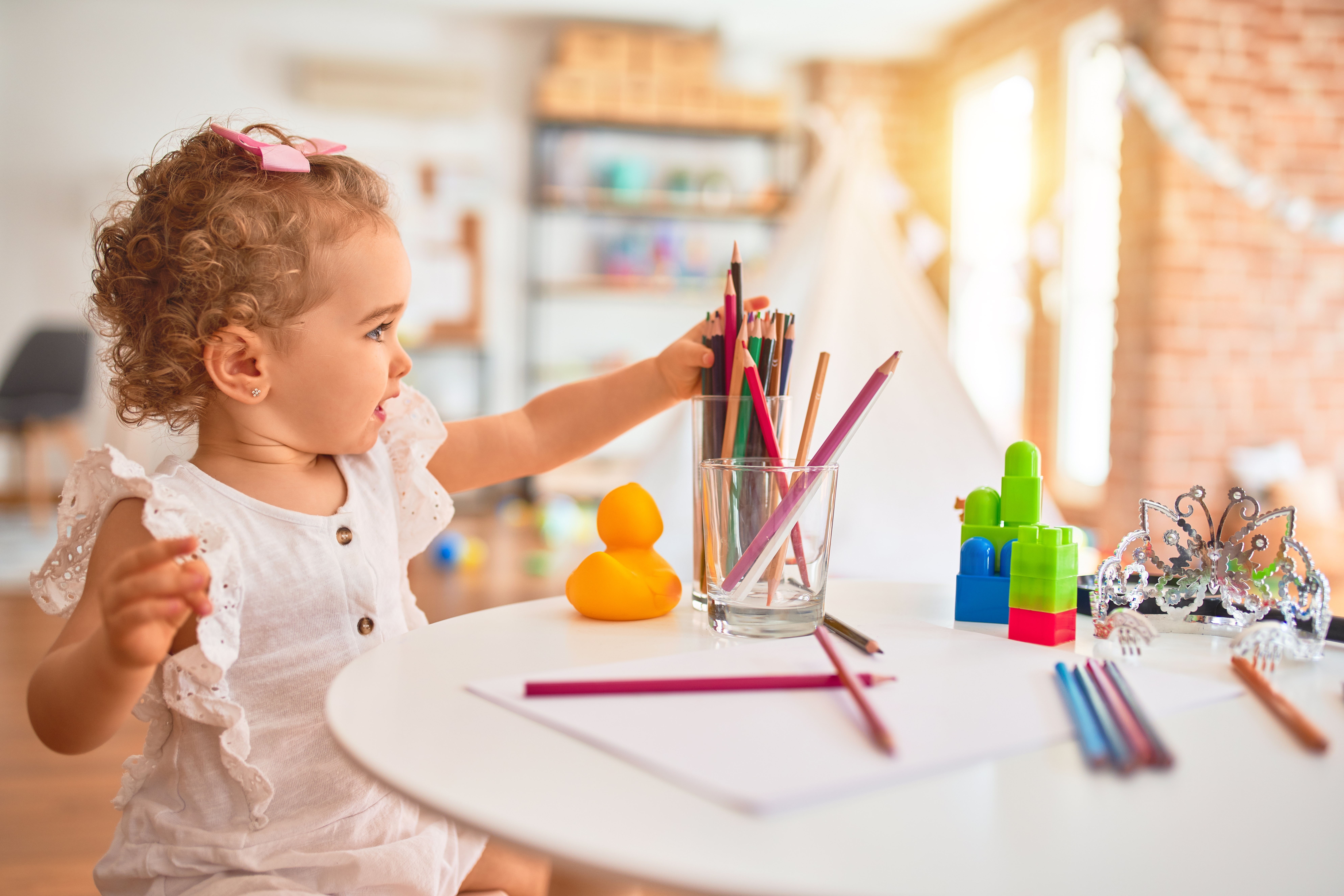 Beautiful caucasian infant playing with toys at colorful playroom. Happy and playful drawing with color pencils at kindergarten.